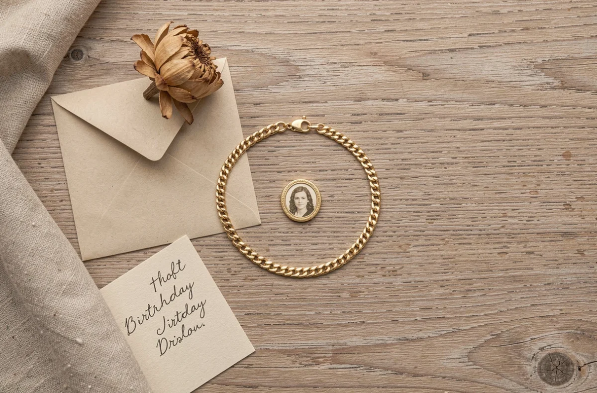 Bracelet photo doré personnalisé pour anniversaire posé en flat lay avec une carte manuscrite et une fleur séchée sur bois rustique
