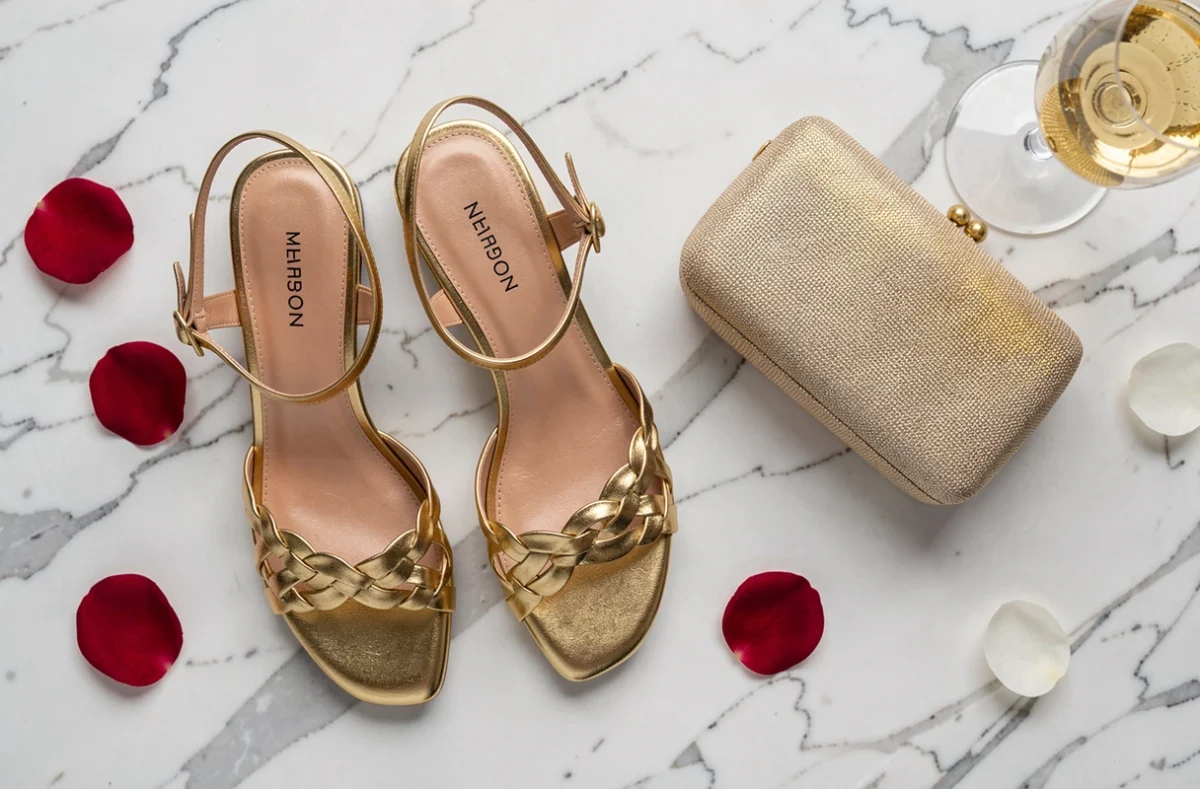Flat-lay de sandales dorées à petit talon avec pochette et champagne sur marbre blanc