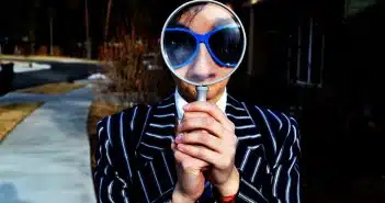 person using magnifying glass enlarging the appearance of his nose and sunglasses